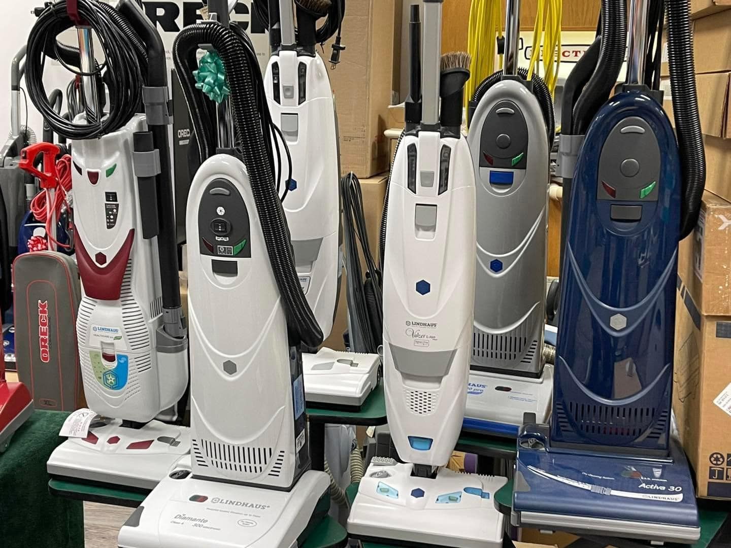 Various upright vacuum cleaners on display in a store; several colors visible, white, blue, red.