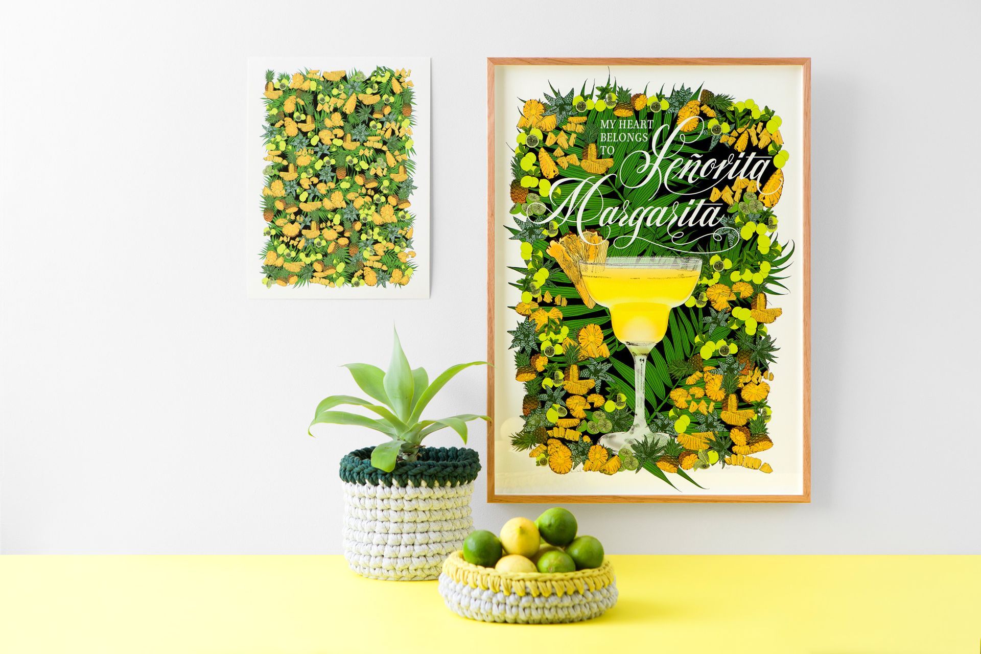 Yellow floral wall art with a framed cocktail print, plant, and fruit bowl on a white and yellow table