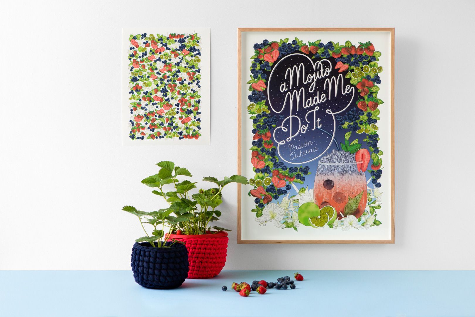 Framed floral print and potted plants on a light blue shelf with small colorful pebbles and art prints nearby