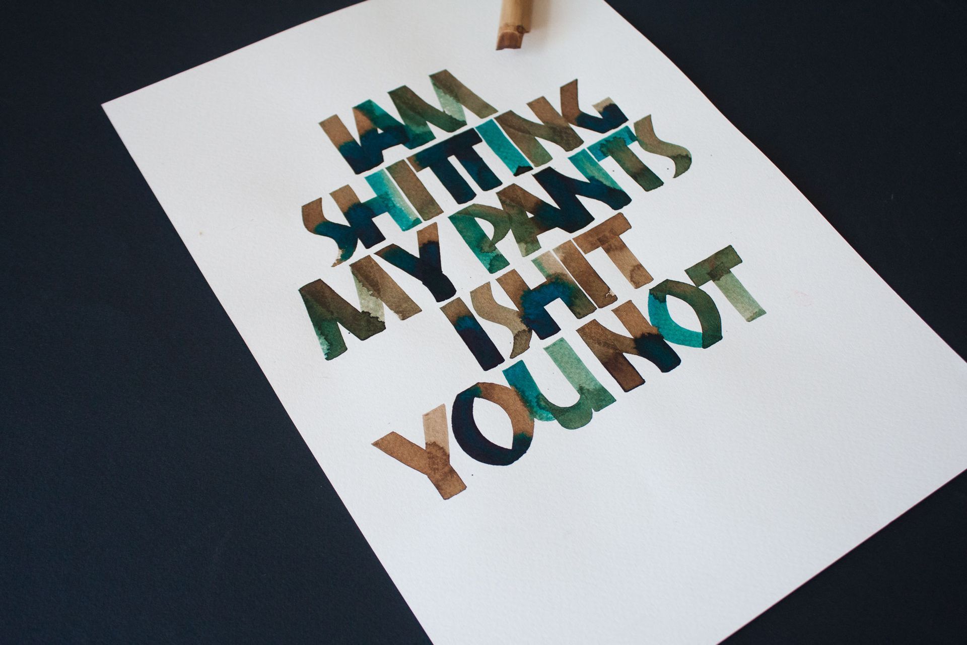 A white piece of paper on a dark surface features bold, block lettering in shades of green and brown reading: