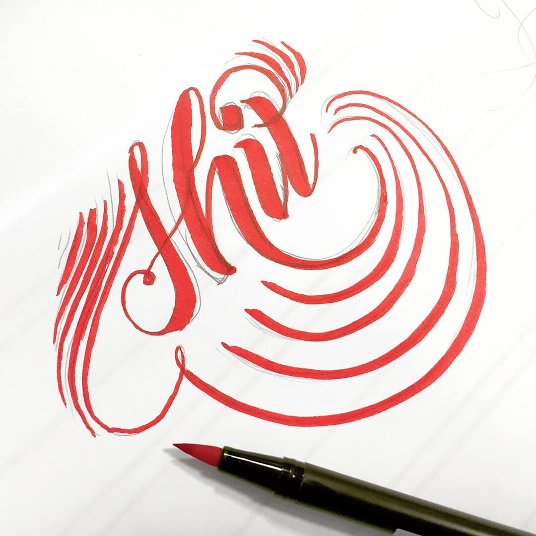 A calligraphy pen rests next to elegant red cursive lettering reading