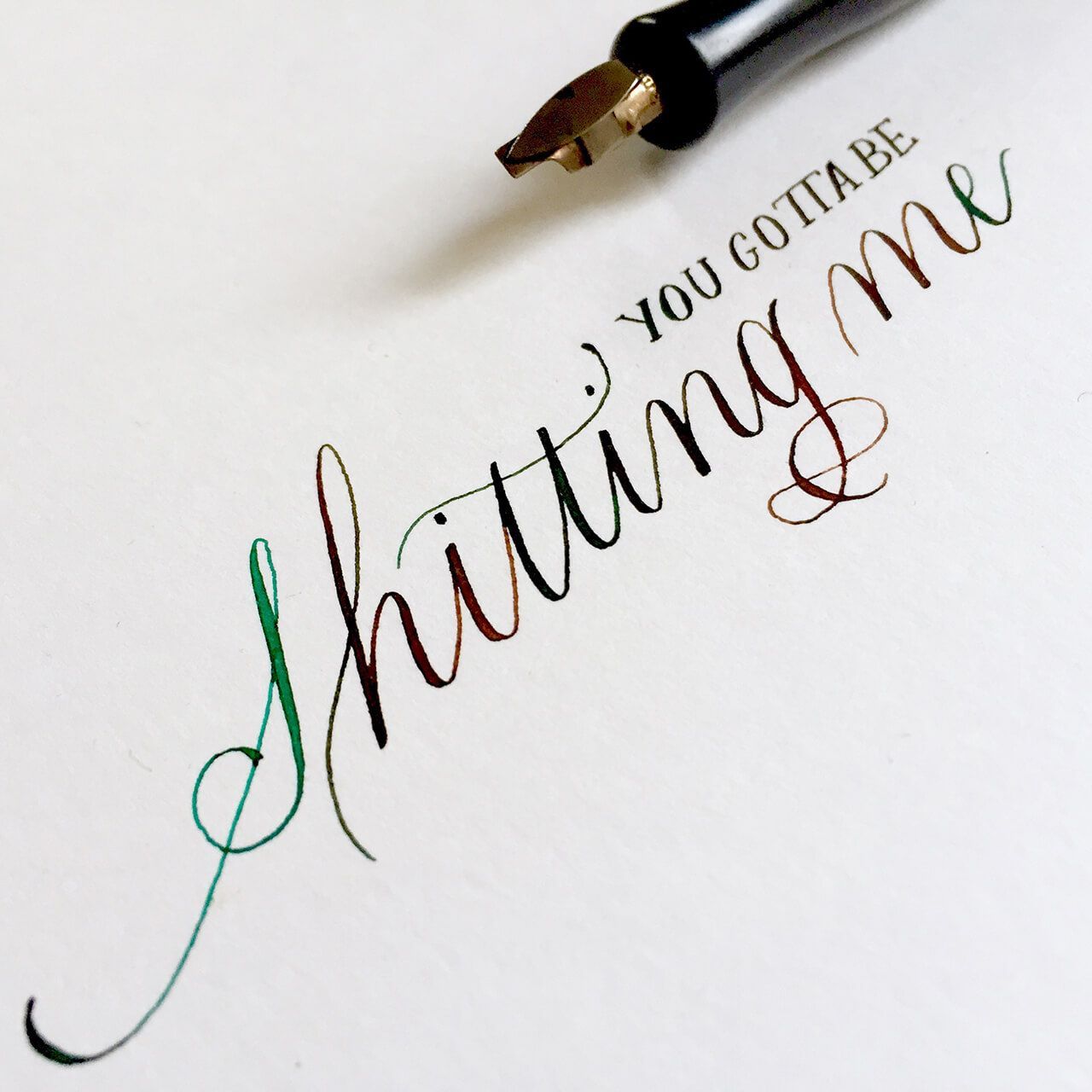 A calligraphy pen resting above elegant, multicolored cursive writing that reads