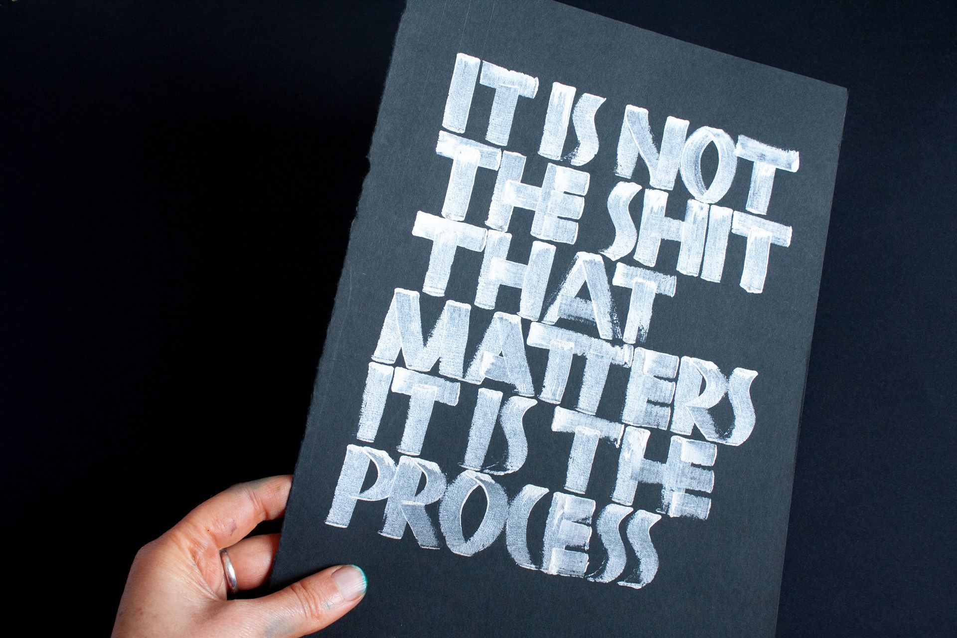 Hand holding a black paper with the white text: