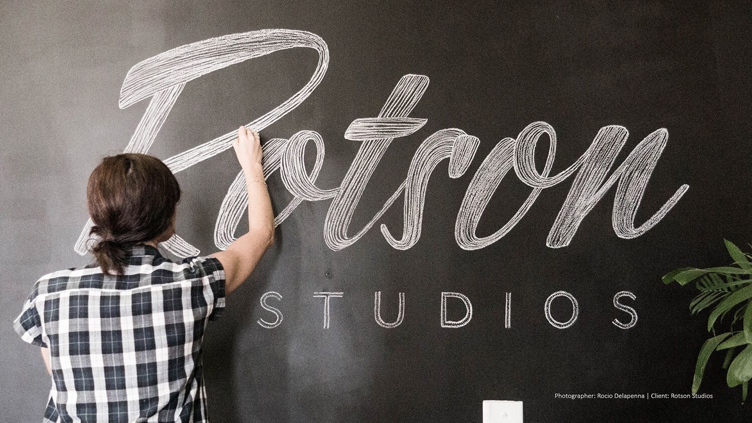 Person writing on a chalkboard wall with “Rotson Studios” in large script.