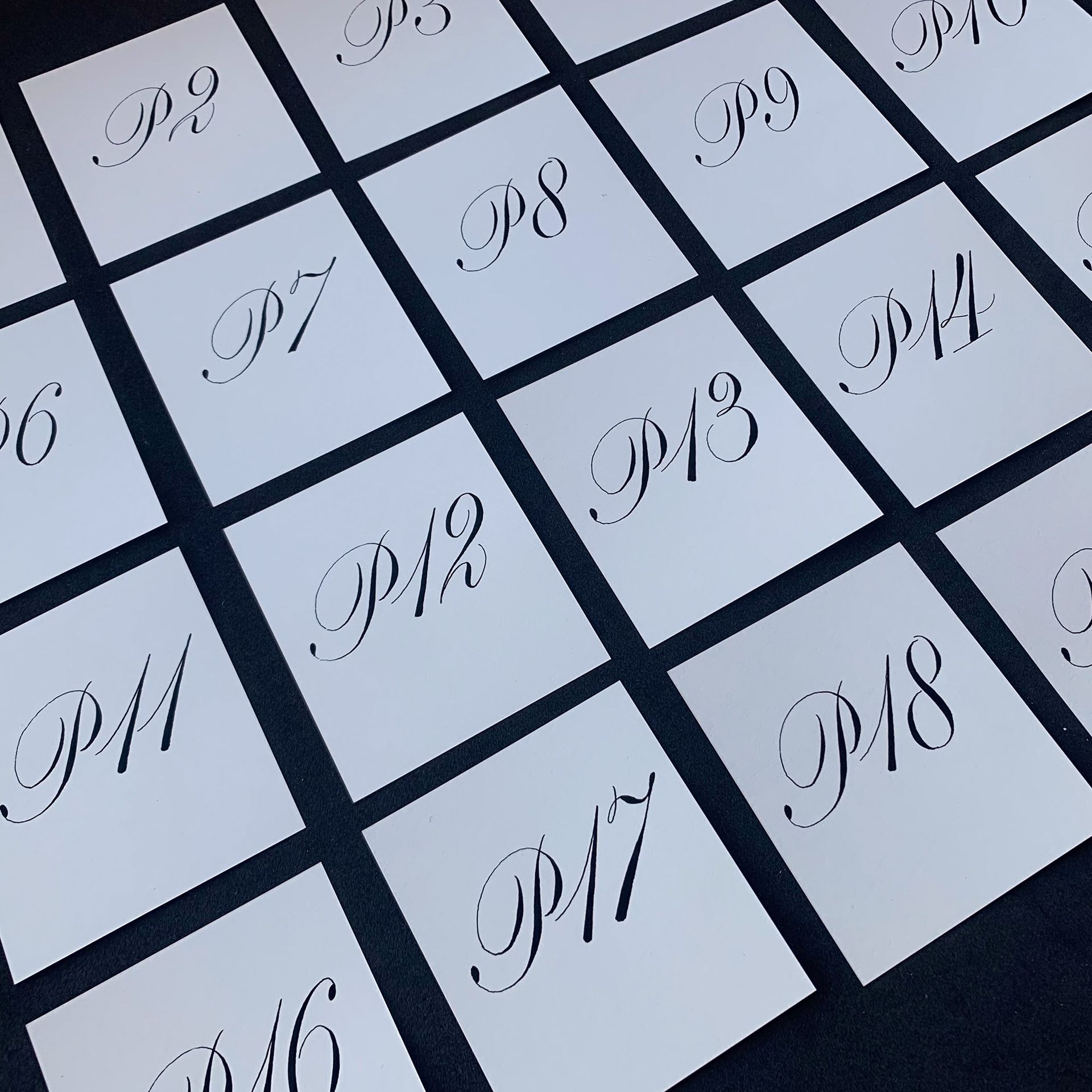 Angled view of white numbered tiles with decorative black script numbers on a dark grid surface