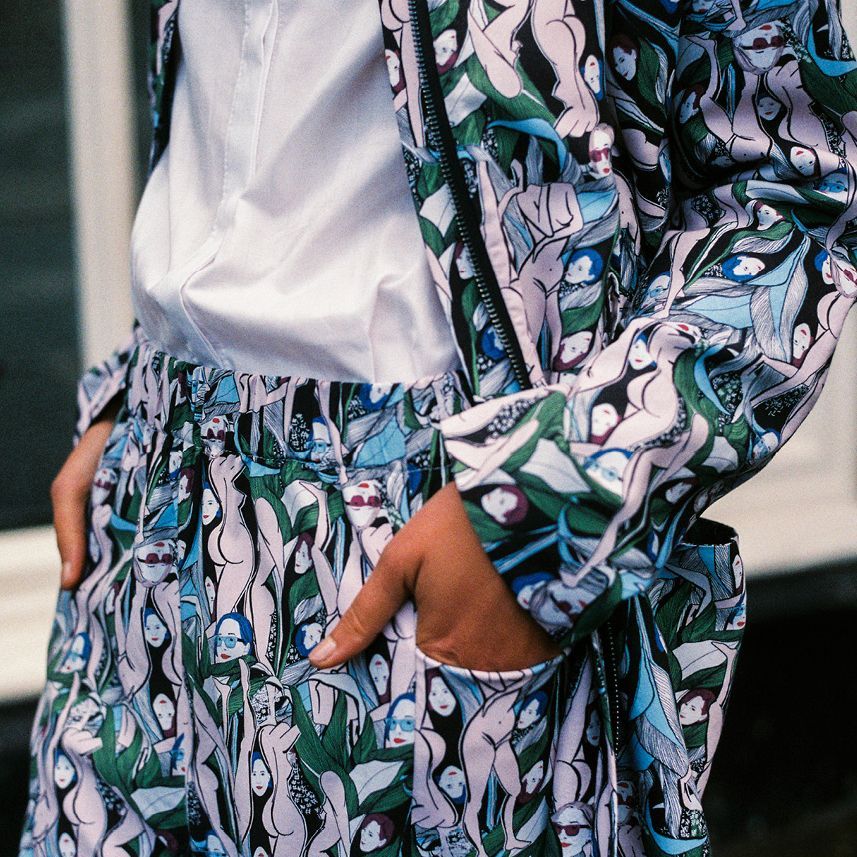 Person in a floral-patterned jacket and pants with a white shirt, hand in pocket.