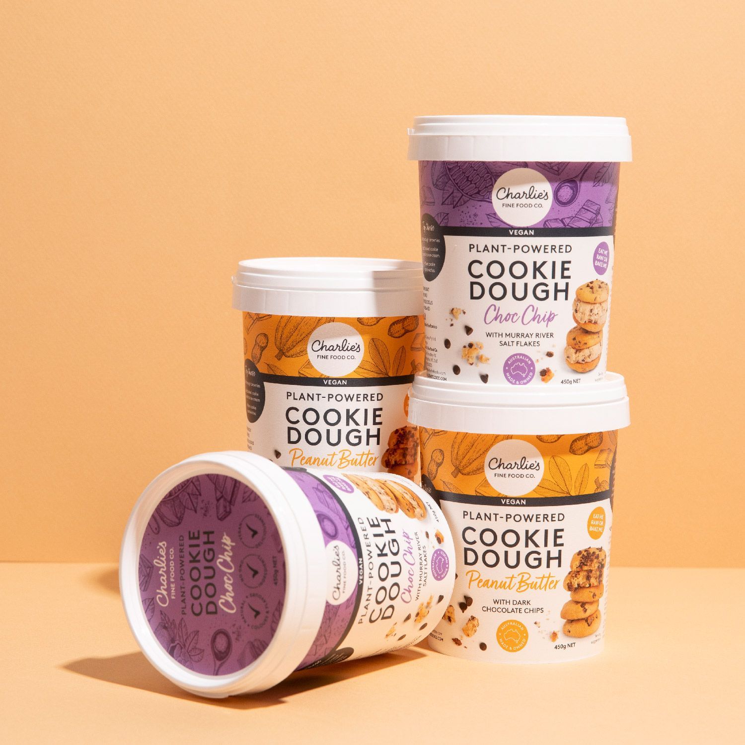 Stacked cookie dough tubs on a peach background, including a purple-lidded tub lying on its side.
