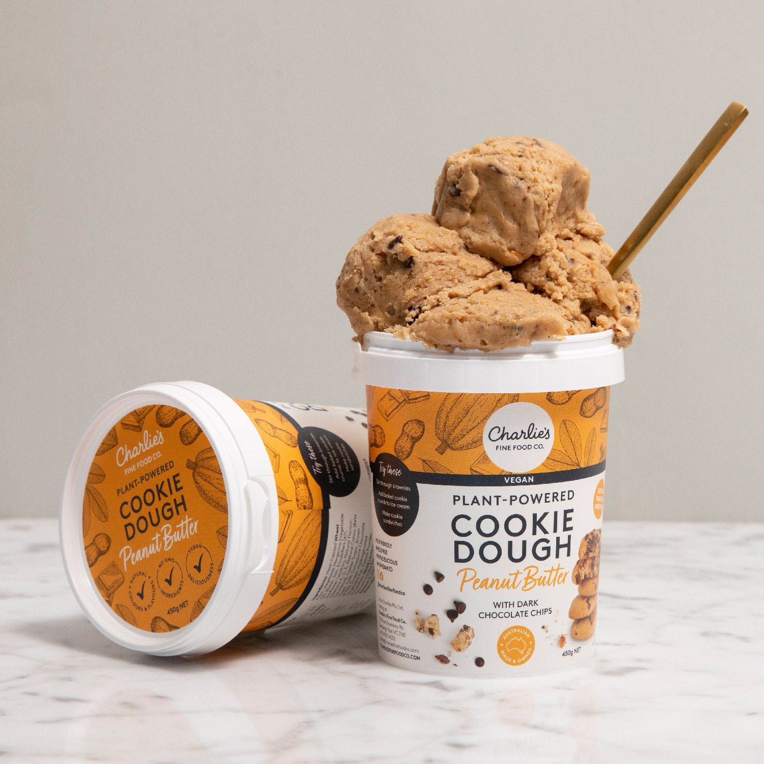 Two cookie dough tubs, one tipped over with dough spilling out and a spoon in a studio setting