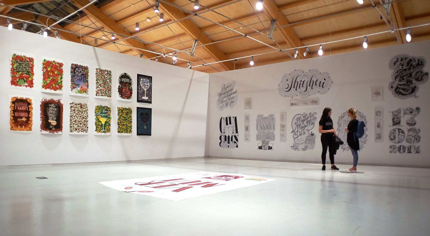 Art gallery with colorful abstract wall pieces and floor installations in a bright room with a wood-beamed ceiling