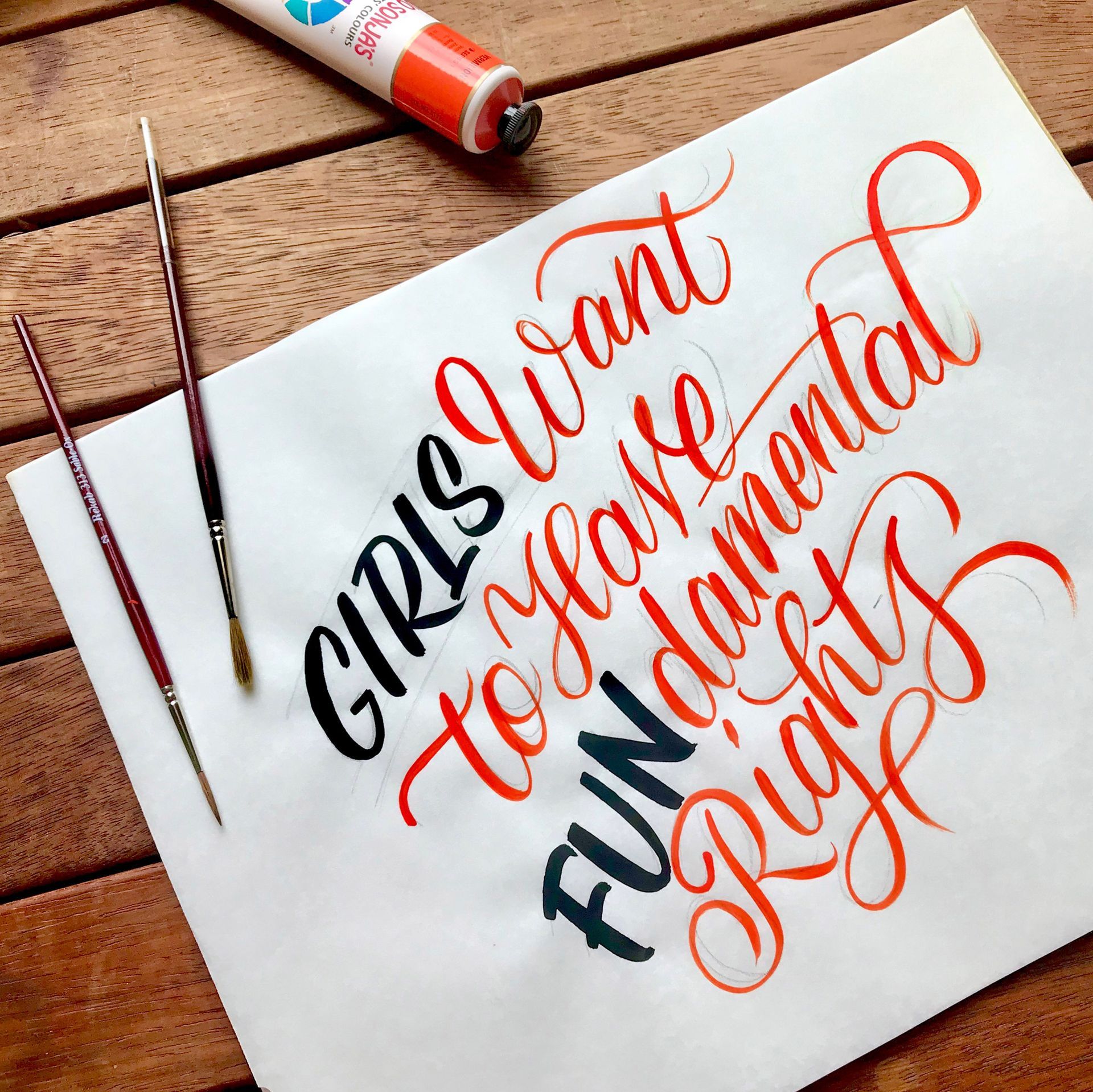 Calligraphy in orange and dark blue on white paper reads