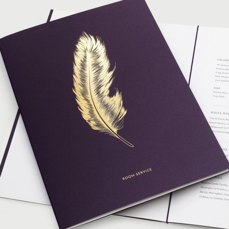 A deep purple hotel room service menu featuring a gold feather illustration and gold text on a white background.