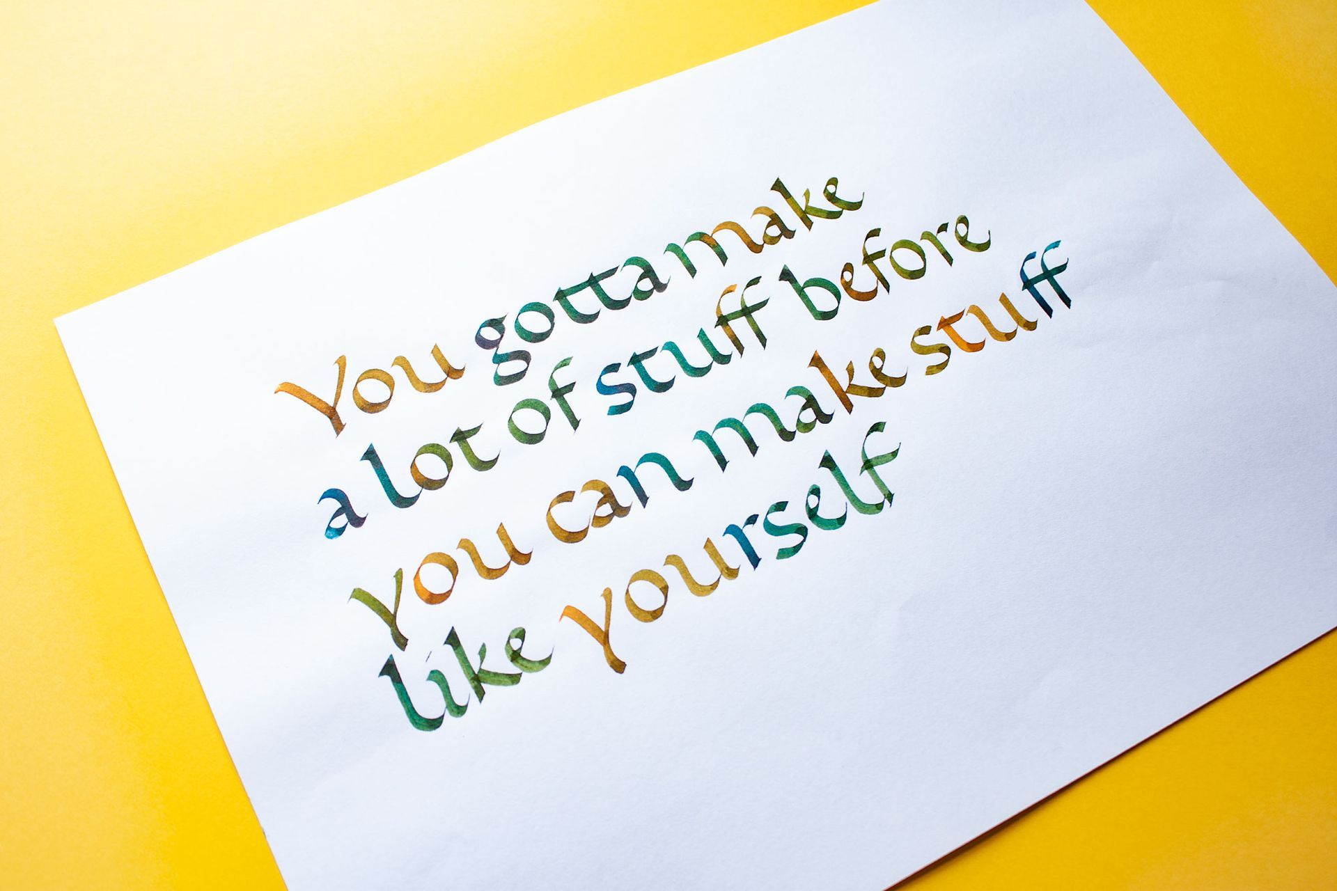Inspirational quote on white paper over a yellow background, with colorful stylized text.