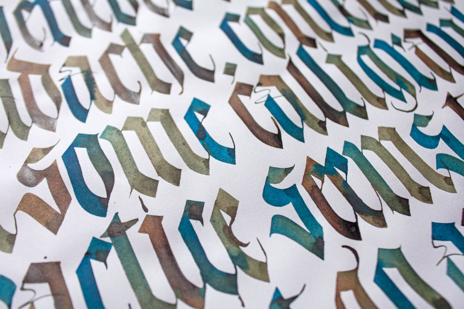 Close-up of ornate calligraphy in gold, teal, and black on white paper.