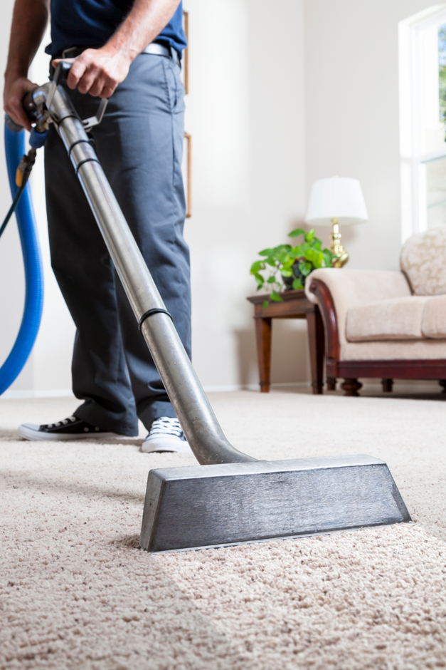 A man is using a commercial carpet cleaner to clean a carpet in a living room.