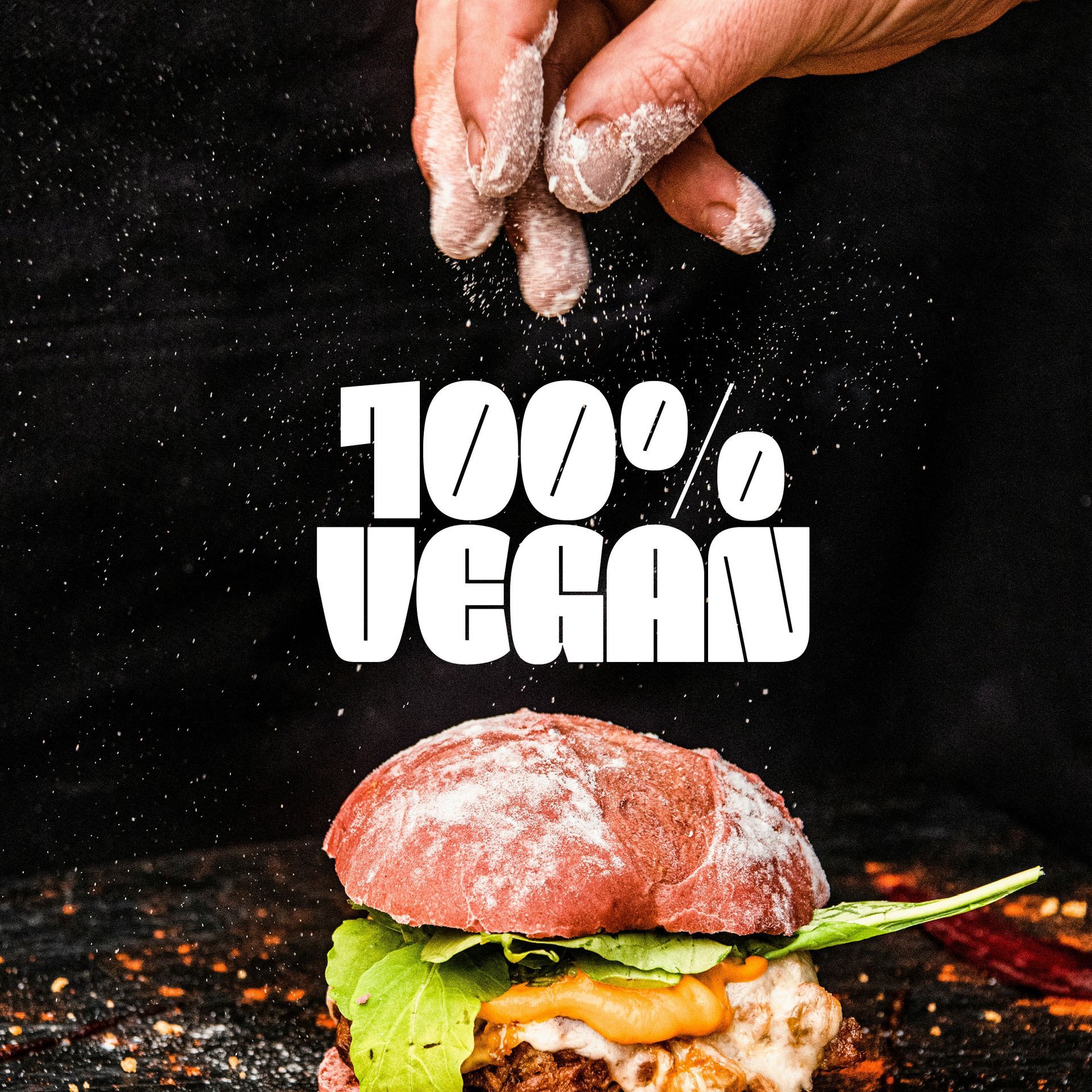 Hands sprinkling flour over a cheeseburger with the words “100% VEGAN” on a black background
