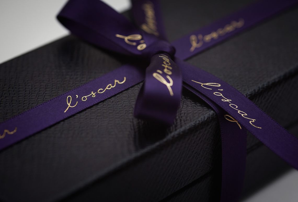 Black gift box wrapped with a purple ribbon and gold script.