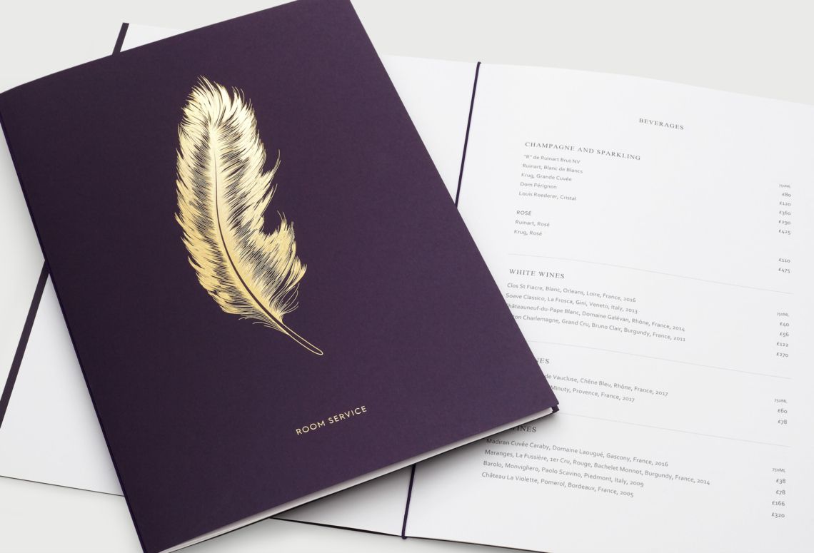 Purple notebook with a gold feather on the cover lying beside an open typed document