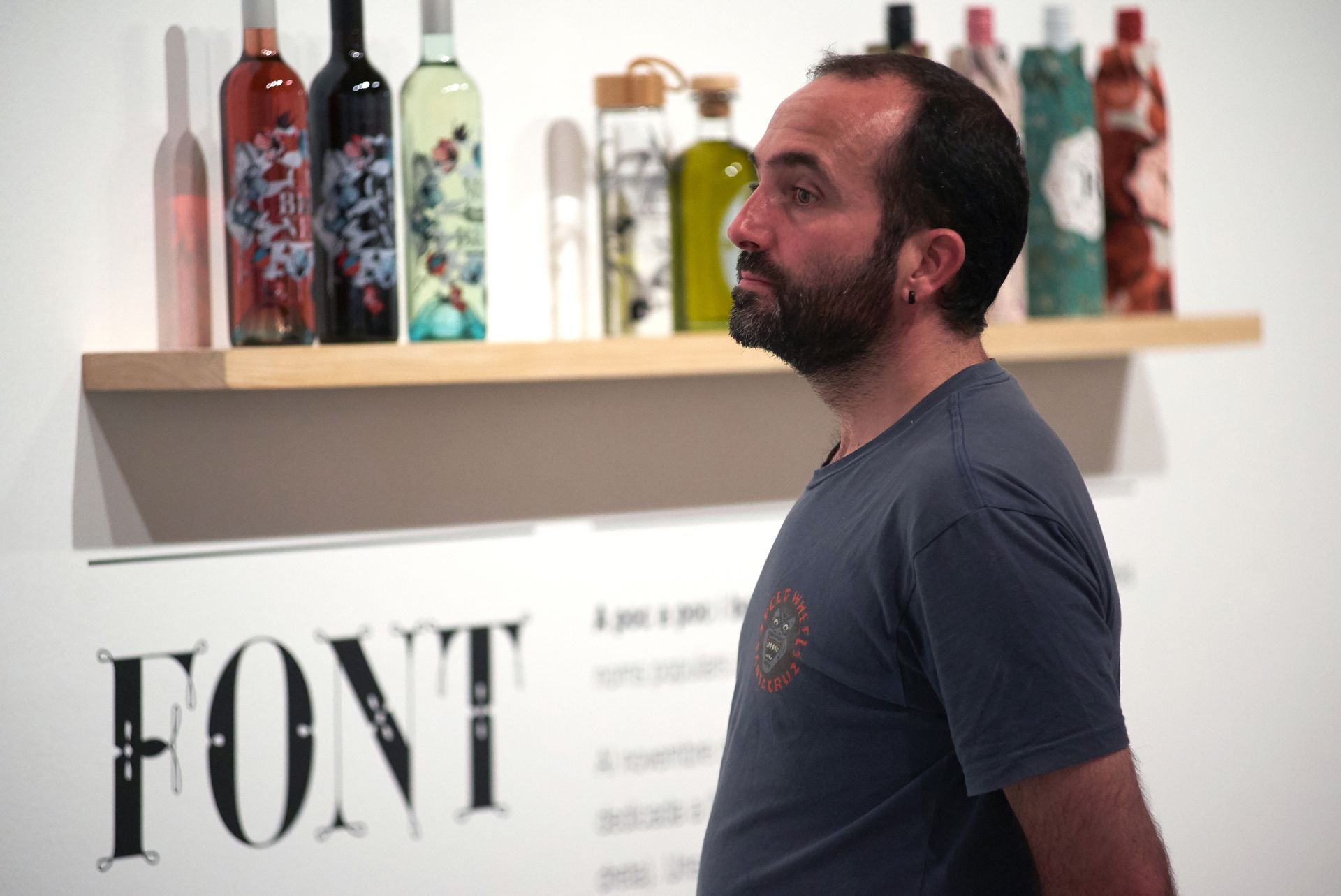Man standing in profile in an art gallery with colorful glass sculptures on a shelf behind him