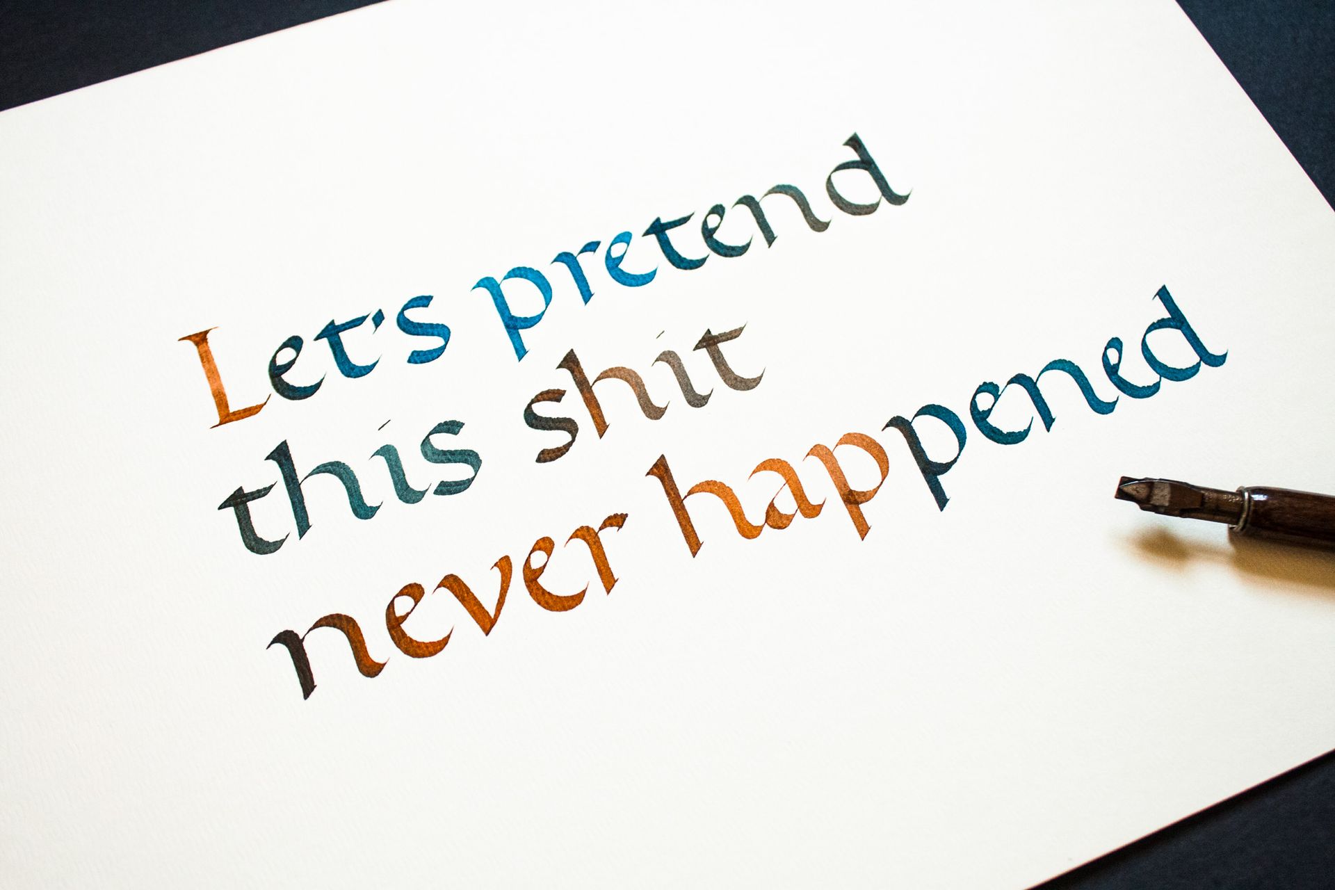 Stylized text reading “Let’s pretend this shit never happened” on white paper with a pen nearby