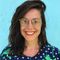 Smiling Maria Montes with glasses and dark hair against a turquoise wall, wearing a navy polka dot shirt