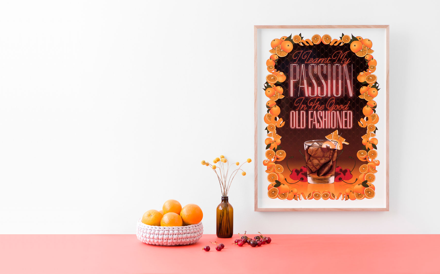 Pink tabletop display with orange flowers, a vase, fruit, and a framed “Fashion” poster on the wall