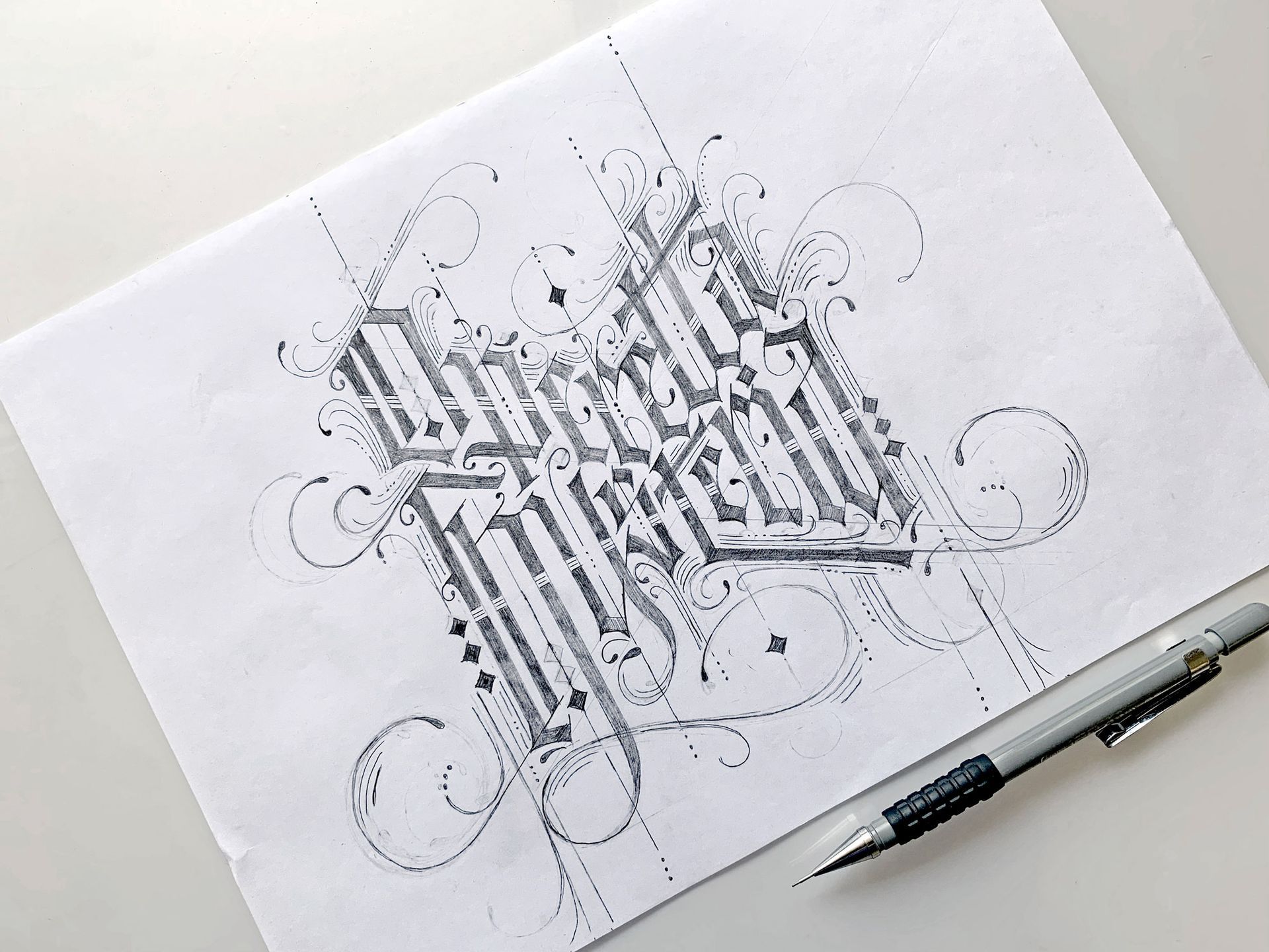 A detailed pencil sketch of elaborate, gothic-style calligraphy on white paper next to a mechanical pencil.