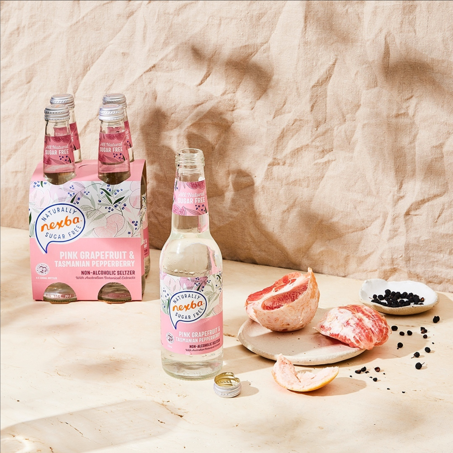 Pink bottled drink set with fruit bowls and berries on a beige cloth backdrop