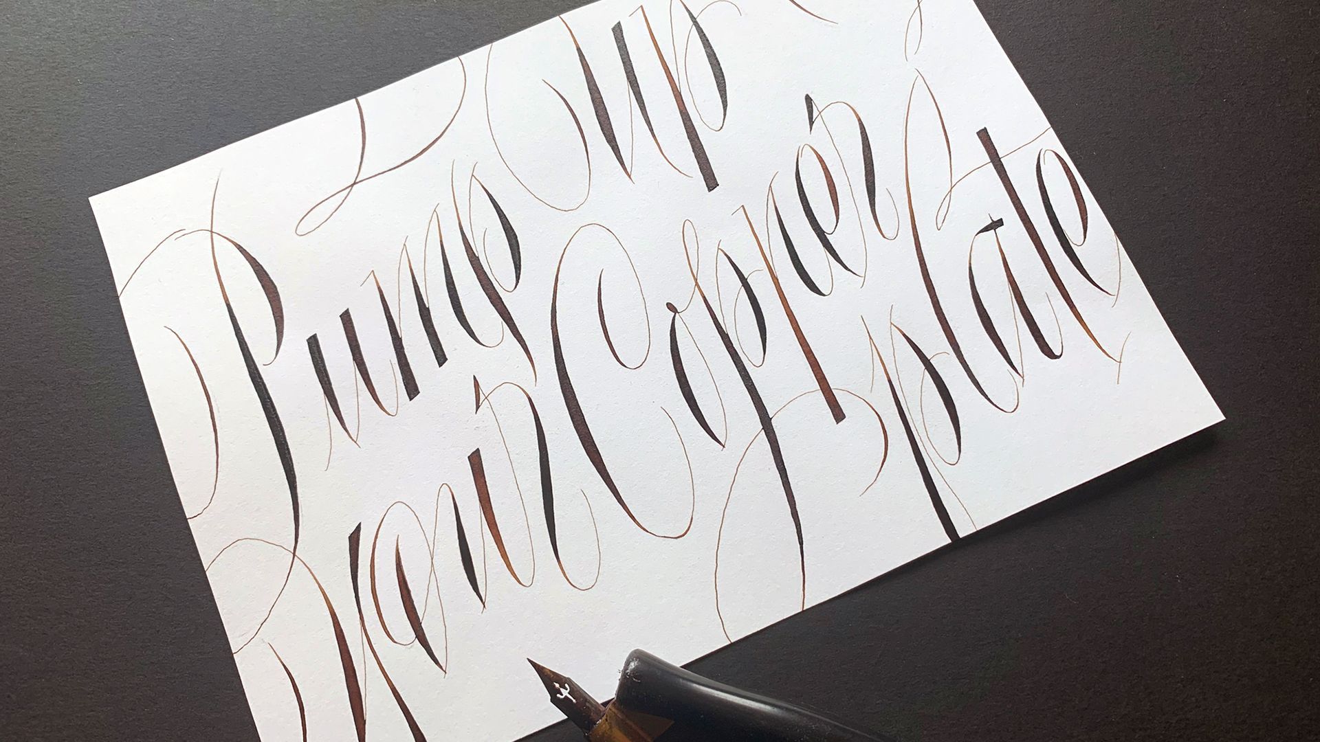 Close-up of a pen practicing cursive calligraphy on white paper with repeated strokes.