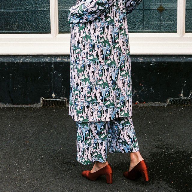 Person in a patterned coat and pants walking on wet pavement in red heels.