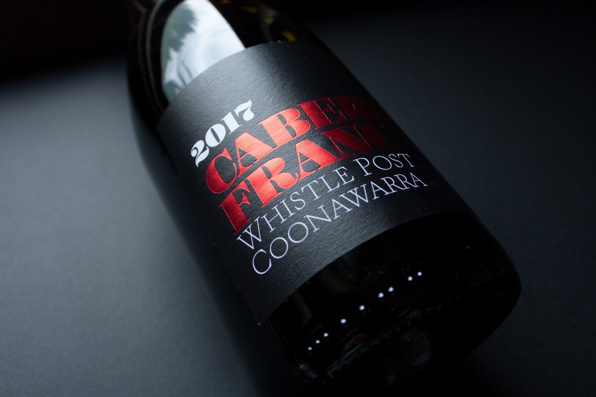 Black wine bottle labeled “1995 LAKE FIRE” on a dark surface, angled in low light
