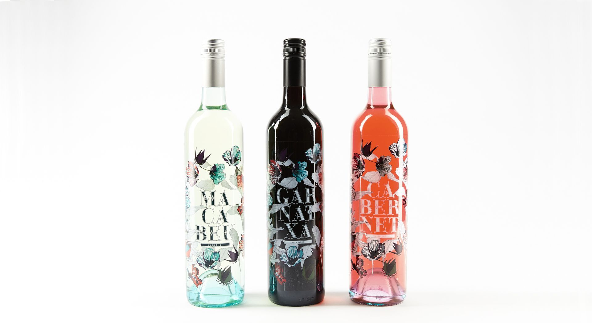 Three wine bottles with floral labels stand against a white background: a white wine, a red wine, and a rosé.