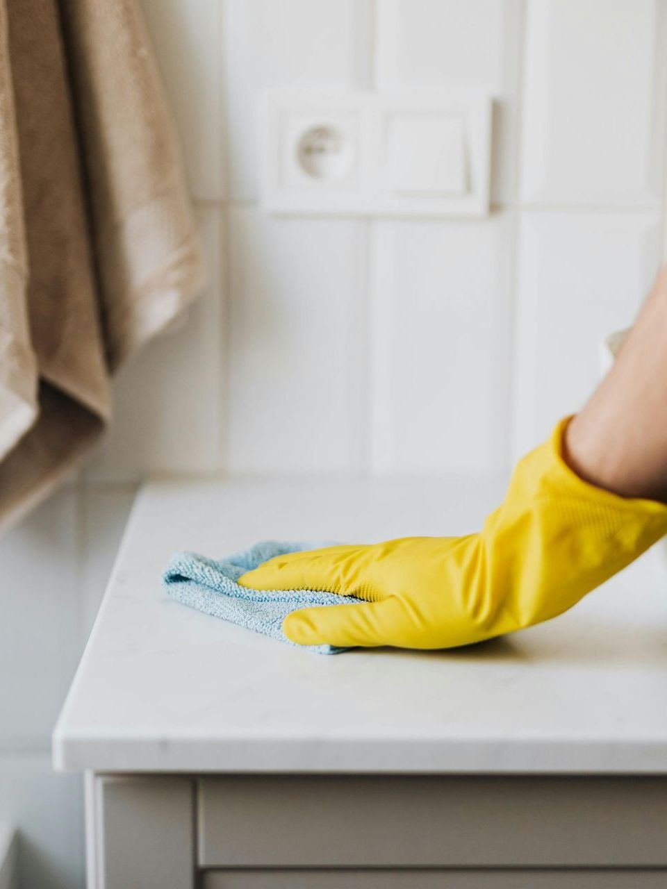 A person wearing yellow rubber gloves is cleaning a counter with a cloth for a end of lease clean.