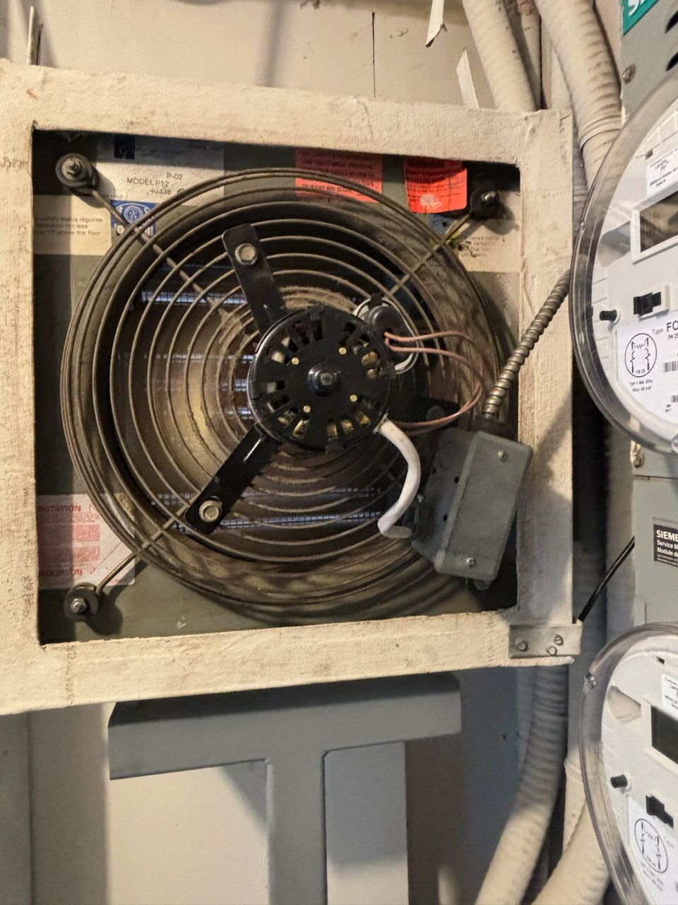 Un ventilateur industriel carré avec une grille de protection, fixé au mur.