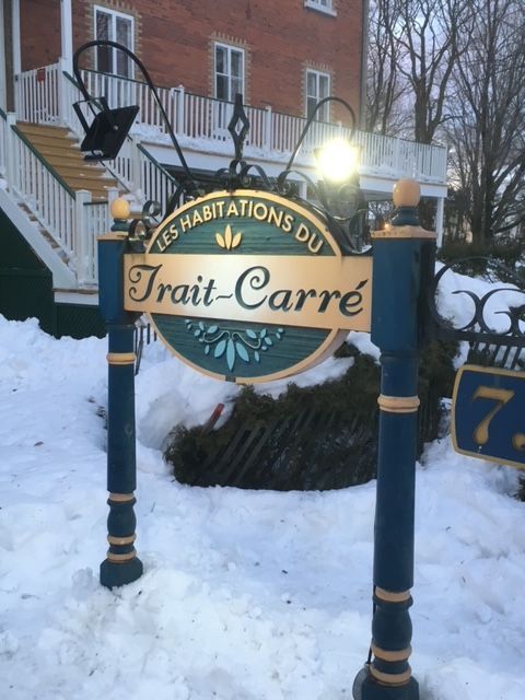 Panneau « Les Habitations du Trait-Carré » avec des poteaux turquoise et or, dans un décor enneigé.