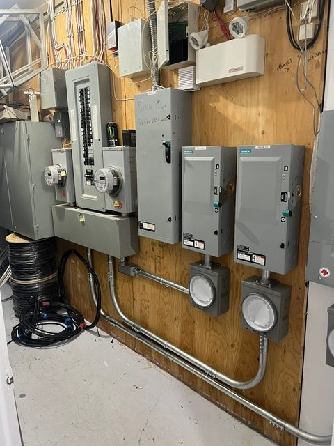 Tableau électrique avec compteurs, disjoncteurs et conduits, monté sur un mur lambrissé.