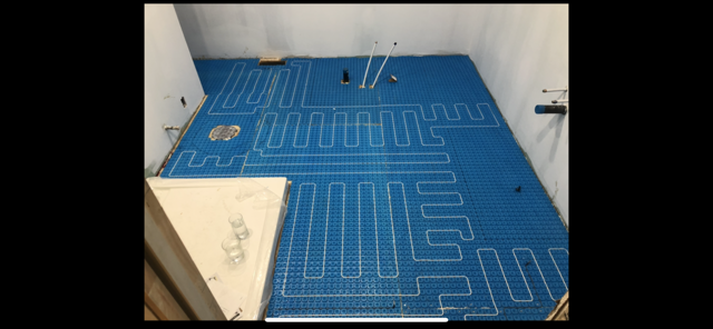 Système de chauffage au sol bleu installé dans une pièce, avec des tuyaux blancs disposés selon un motif.