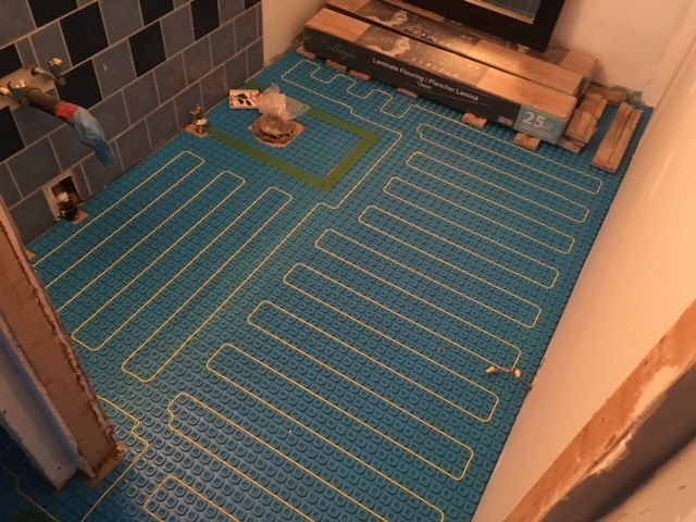 Sol de salle de bains avec tapis chauffant bleu et tuyaux jaunes, prêt pour la pose de carrelage.