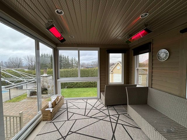 Véranda avec deux radiateurs rouges, vue sur l'extérieur à travers les fenêtres, tapis à motifs et meubles marron.