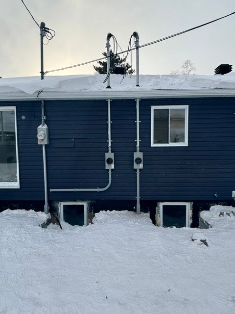 Maison bleue avec conduits électriques, sol enneigé et fenêtres de fondation.