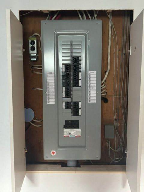 Tableau électrique dans une armoire, avec fils et prises apparents. Porte métallique grise.