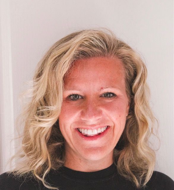 Smiling blonde woman against a plain light background, wearing a black top.