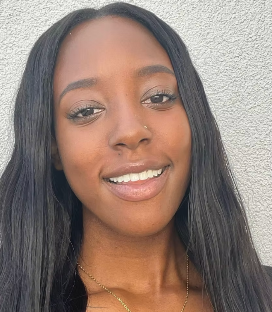 Smiling person with long straight hair against a light textured wall.