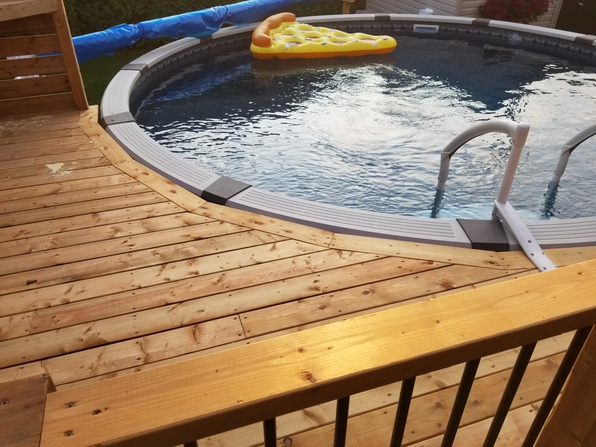 Une piscine avec un flotteur à pizza à l'intérieur se trouve sur une terrasse en bois.