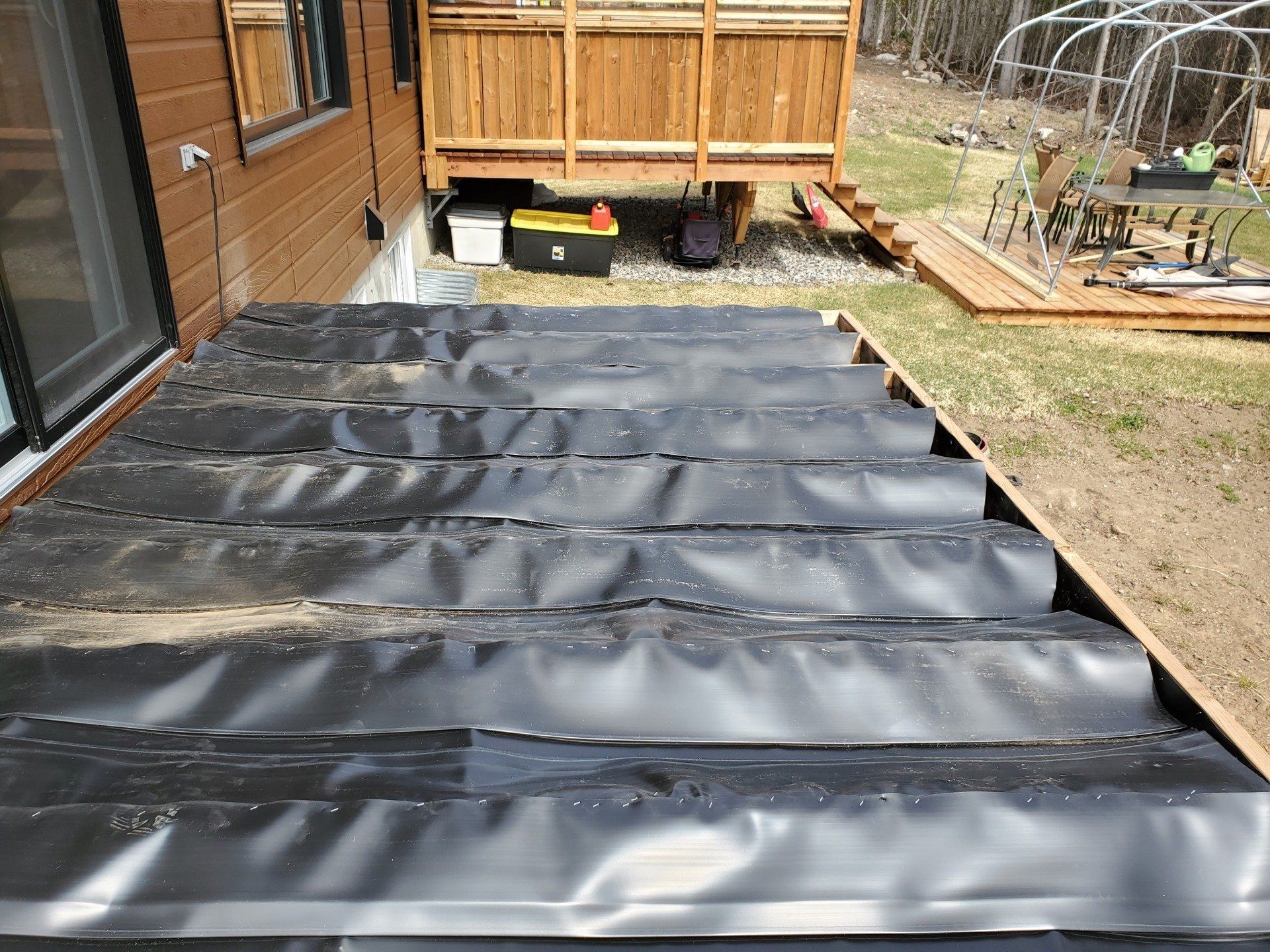 Une bâche noire recouvre une terrasse en bois dans une cour arrière.
