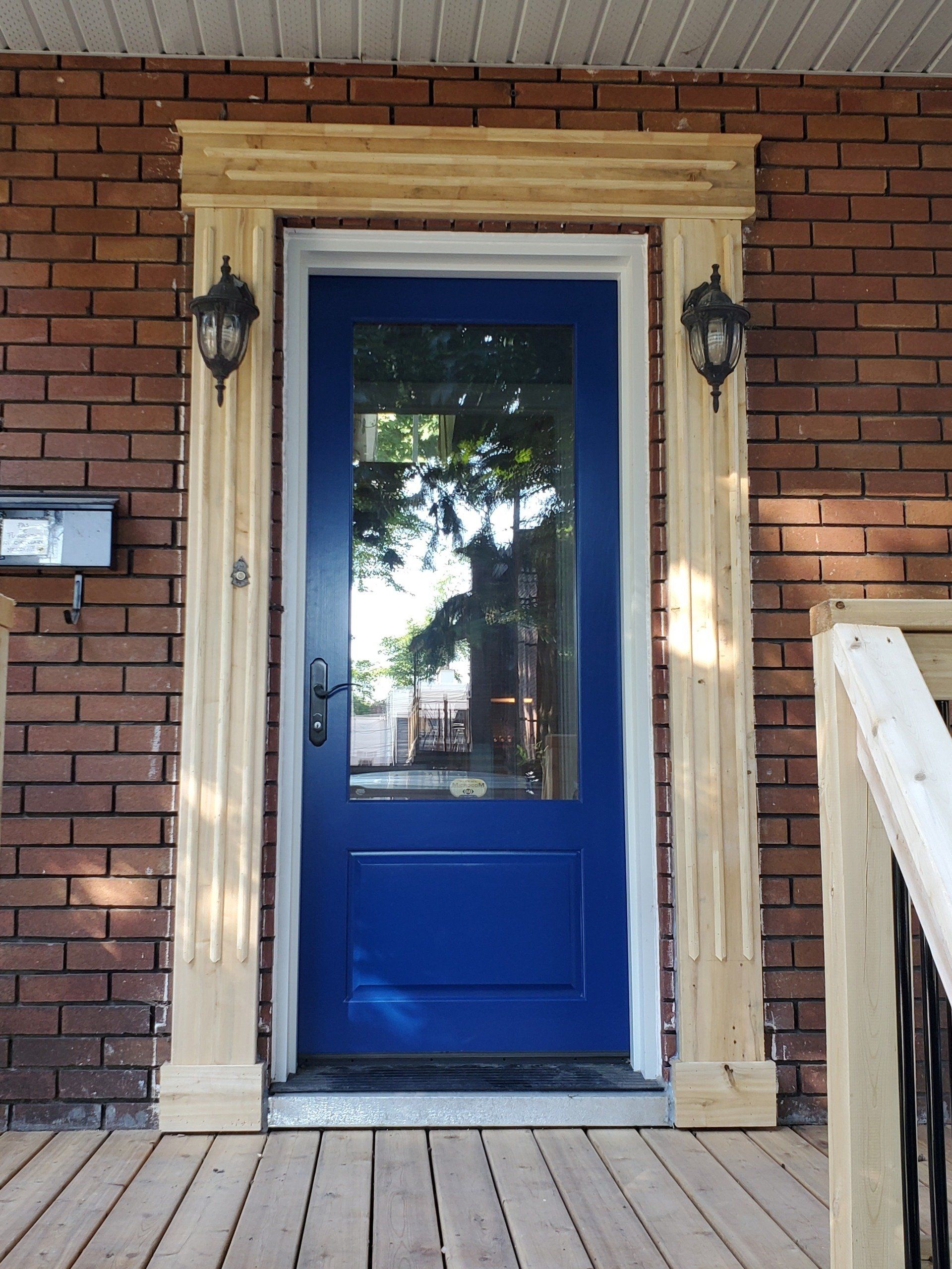 Une porte bleue avec une fenêtre en verre se trouve sur une maison en briques