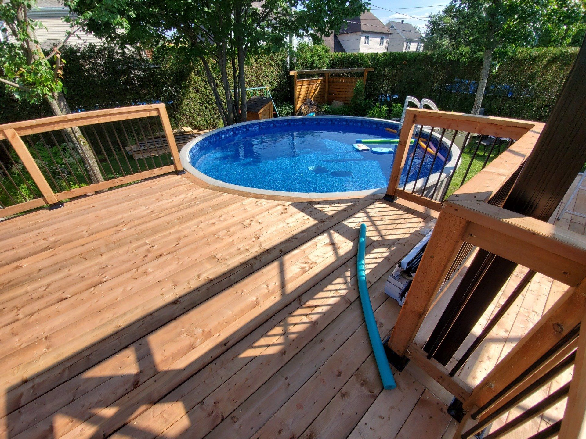 Une terrasse en bois avec une piscine en arrière-plan