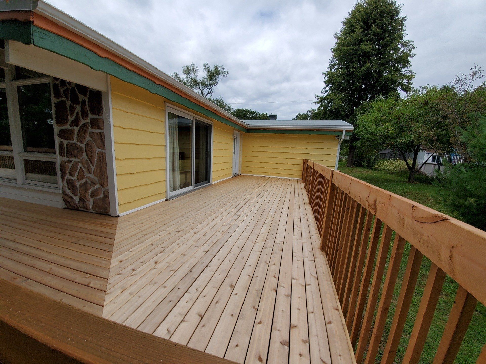 Une grande terrasse en bois se trouve devant une maison jaune.