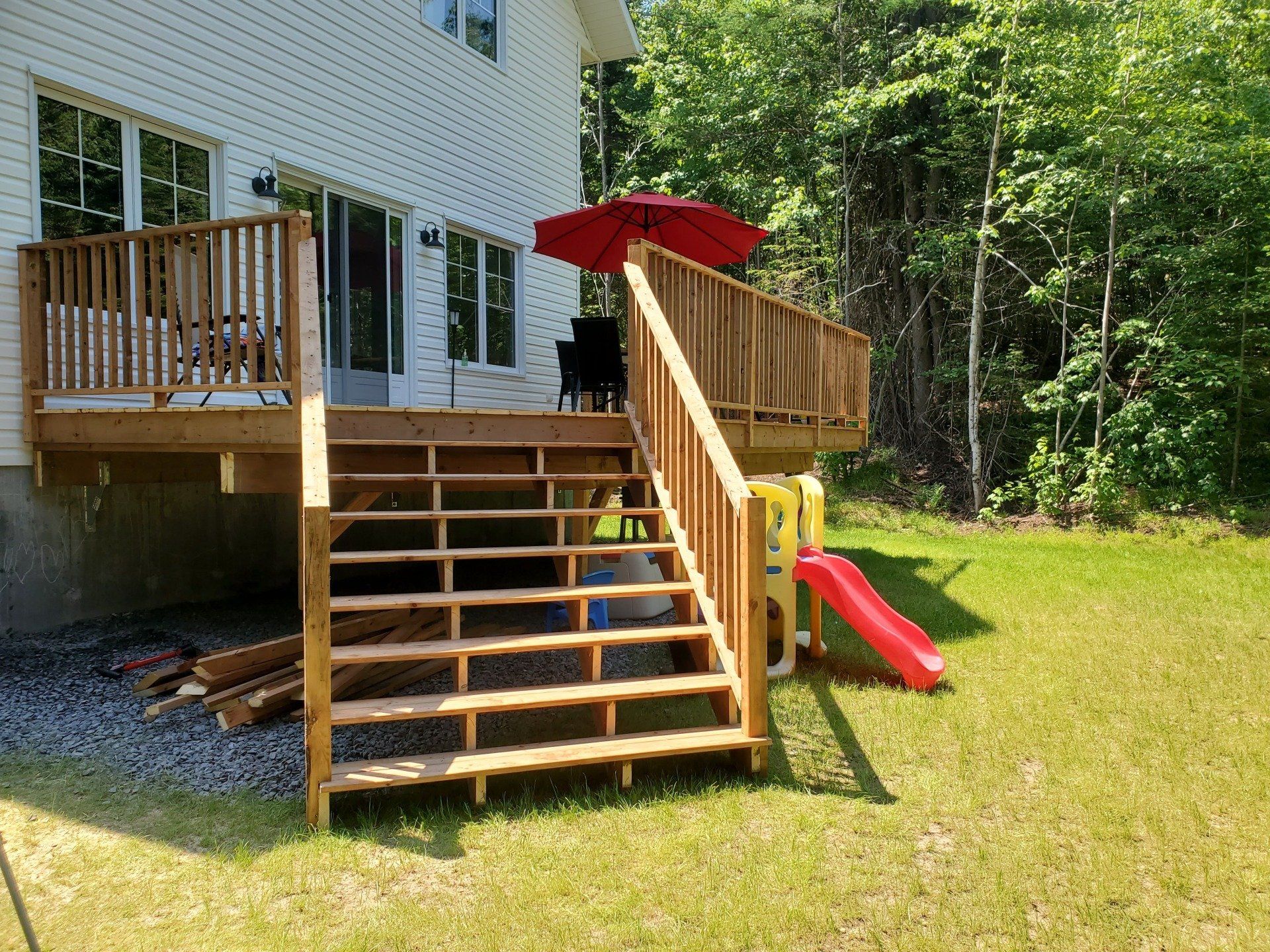 Une terrasse en bois avec des escaliers et un parasol rouge