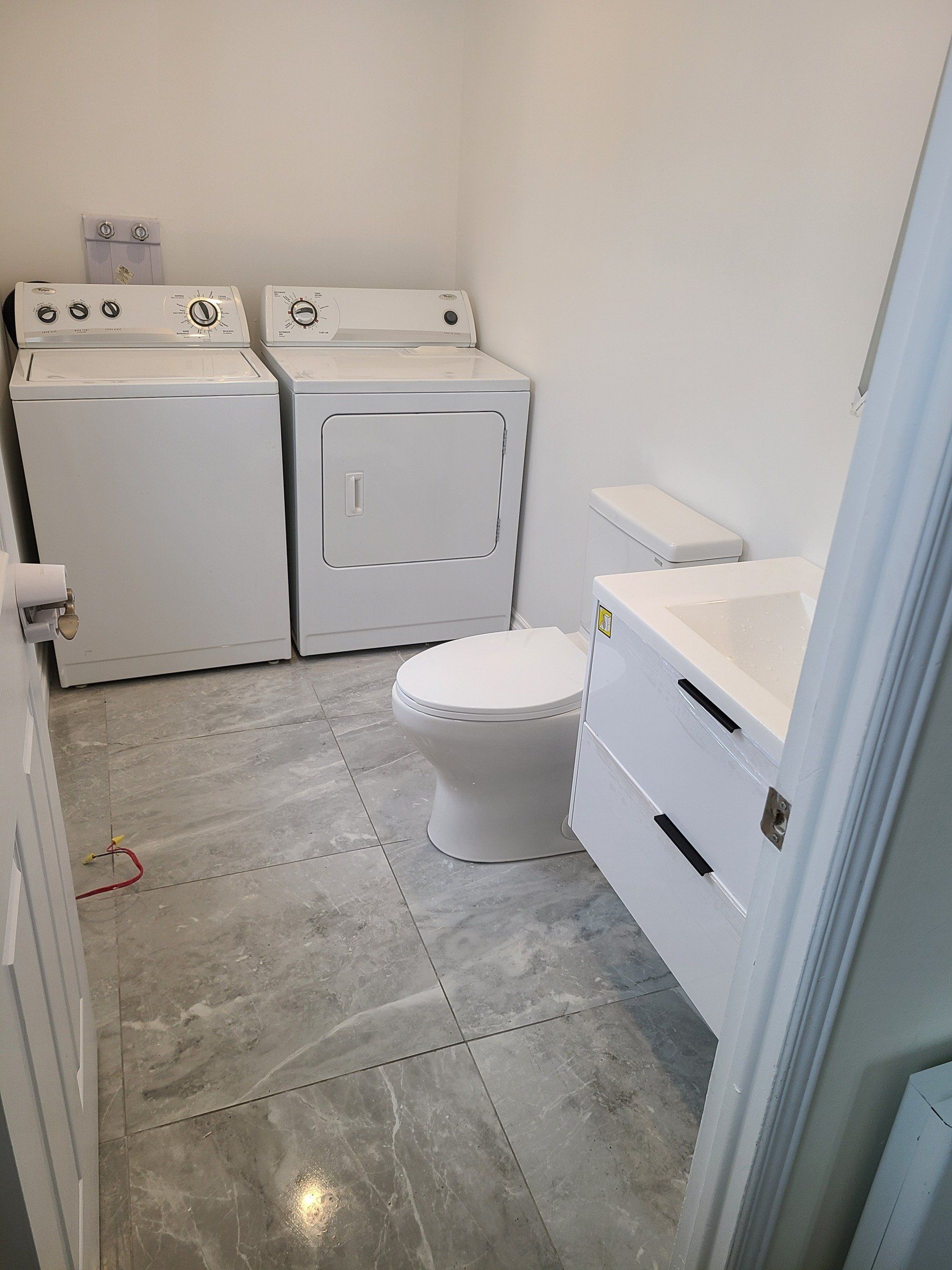 Une buanderie avec laveuse, sécheuse, toilettes et lavabo.