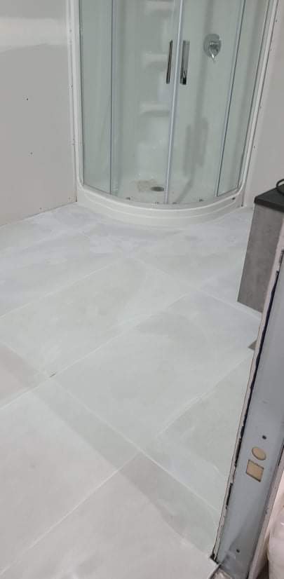 Une salle de bain avec une cabine de douche et un sol en carrelage blanc.